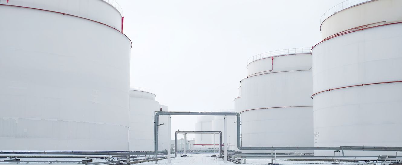 Große weiße Lagertanks in einem verschneiten Industriegebiet mit bewölktem Himmel.